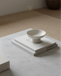 White ceramic bowl on a stack of books on a light-colored surface with a neutral background